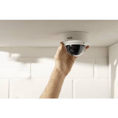 Une main installe une caméra de surveillance au plafond blanc d'une pièce aux murs blancs.