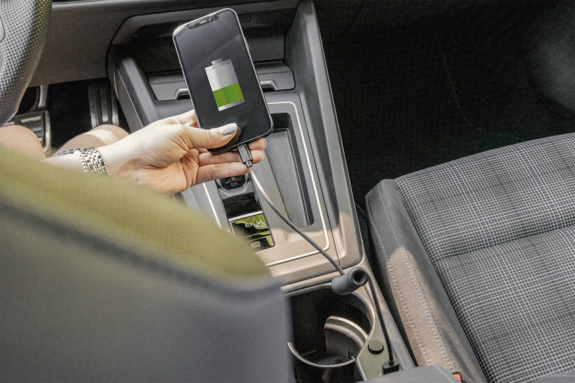 Un smartphone est en train de se charger dans une voiture. L'écran affiche une batterie partiellement chargée.