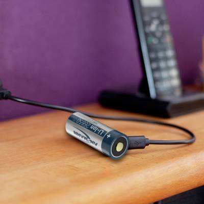 Un téléphone est en cours de chargement sur une table, avec un adaptateur de batterie AA connecté via un câble USB.