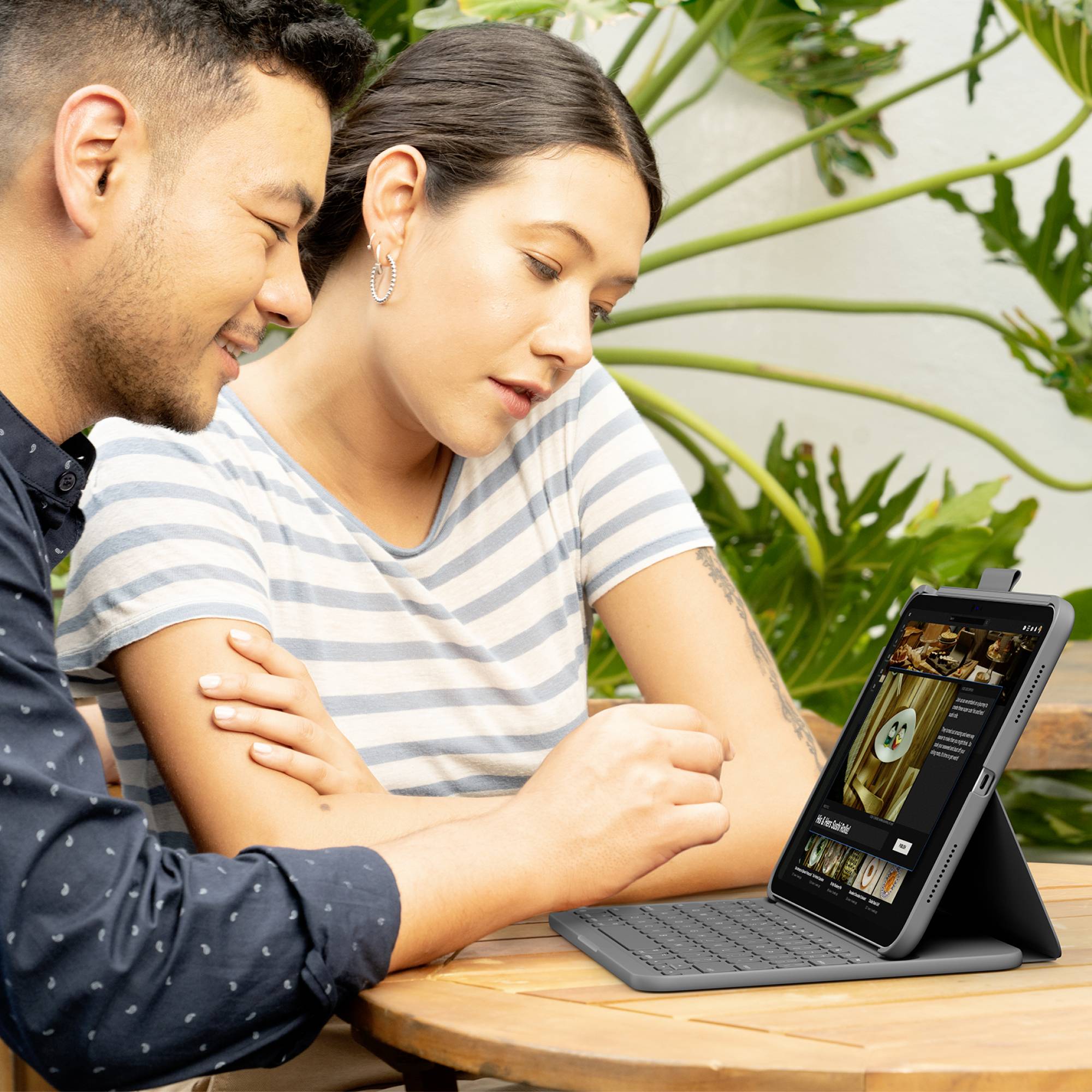Un homme et une femme examinent ensemble une tablette numérique installée sur un support de clavier. Ils semblent être plongés dans une conversation.