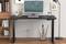 Un bureau moderne avec un écran, un clavier et divers articles de bureau est placé dans un bureau avec des étagères et une lampe.