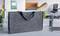 Un sac de documents gris est ouvert sur un bureau. À l'intérieur se trouvent des rouleaux de papier et des documents. En arrière-plan, on distingue des articles de bureau et une chaise floue.