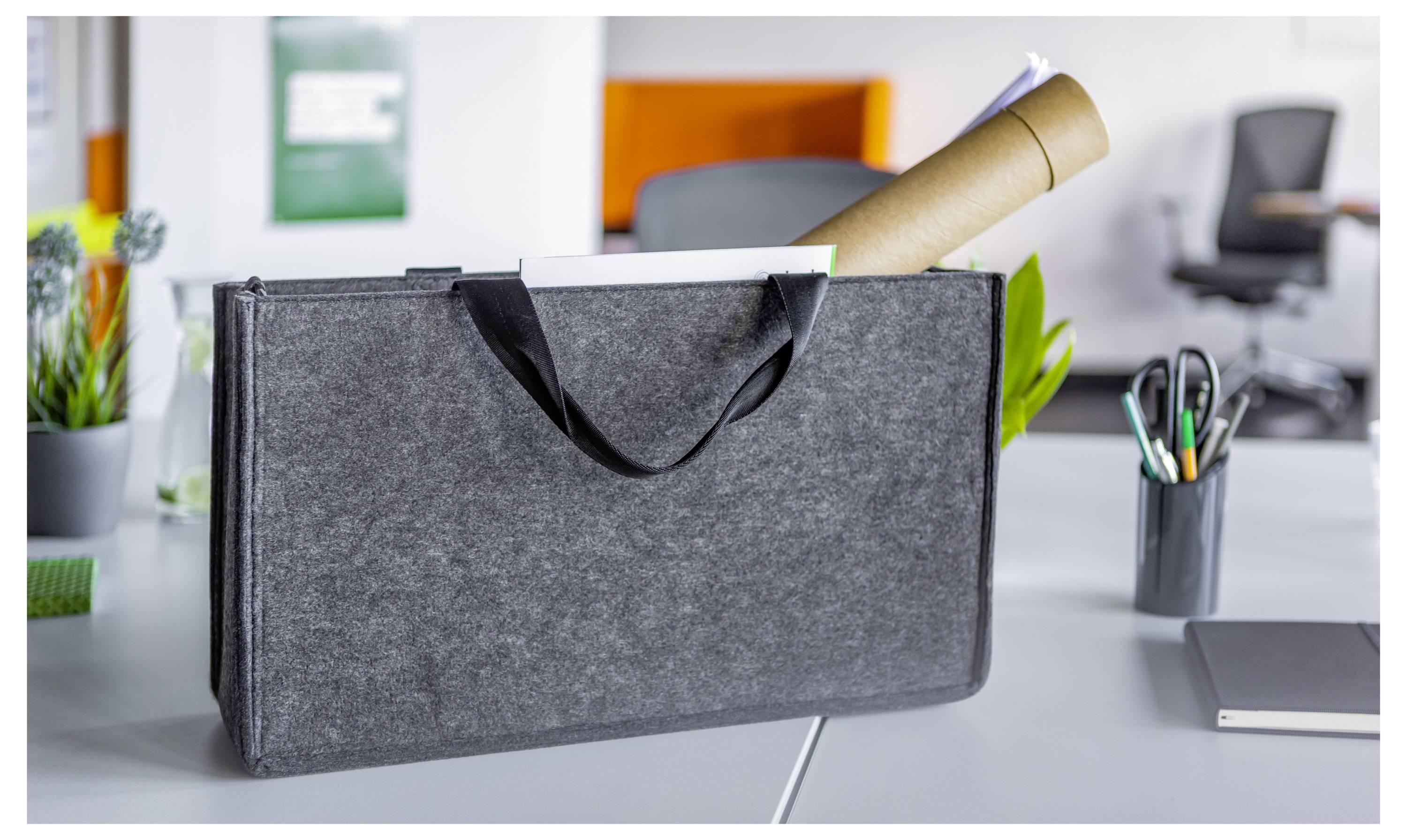 Un sac de documents en feutre avec des poignées noires repose sur un bureau de bureau, avec une affiche enroulée qui dépasse, suggérant un étui de présentation ou de rangement portable.