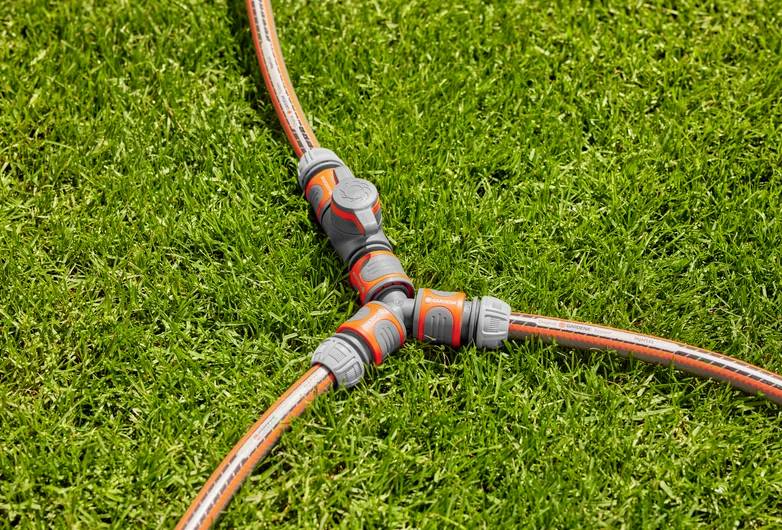 Un connecteur de tuyau à trois voies relie trois tuyaux d'arrosage, formant une forme en Y sur l'herbe verte, facilitant plusieurs écoulements d'eau.