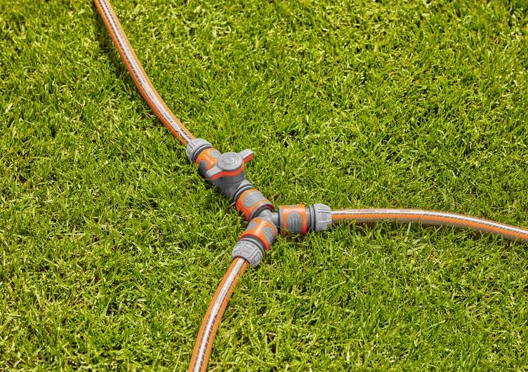 'Pelouse avec un connecteur de tuyau d'arrosage en Y, reliant trois tuyaux oranges sur de l'herbe verte.'