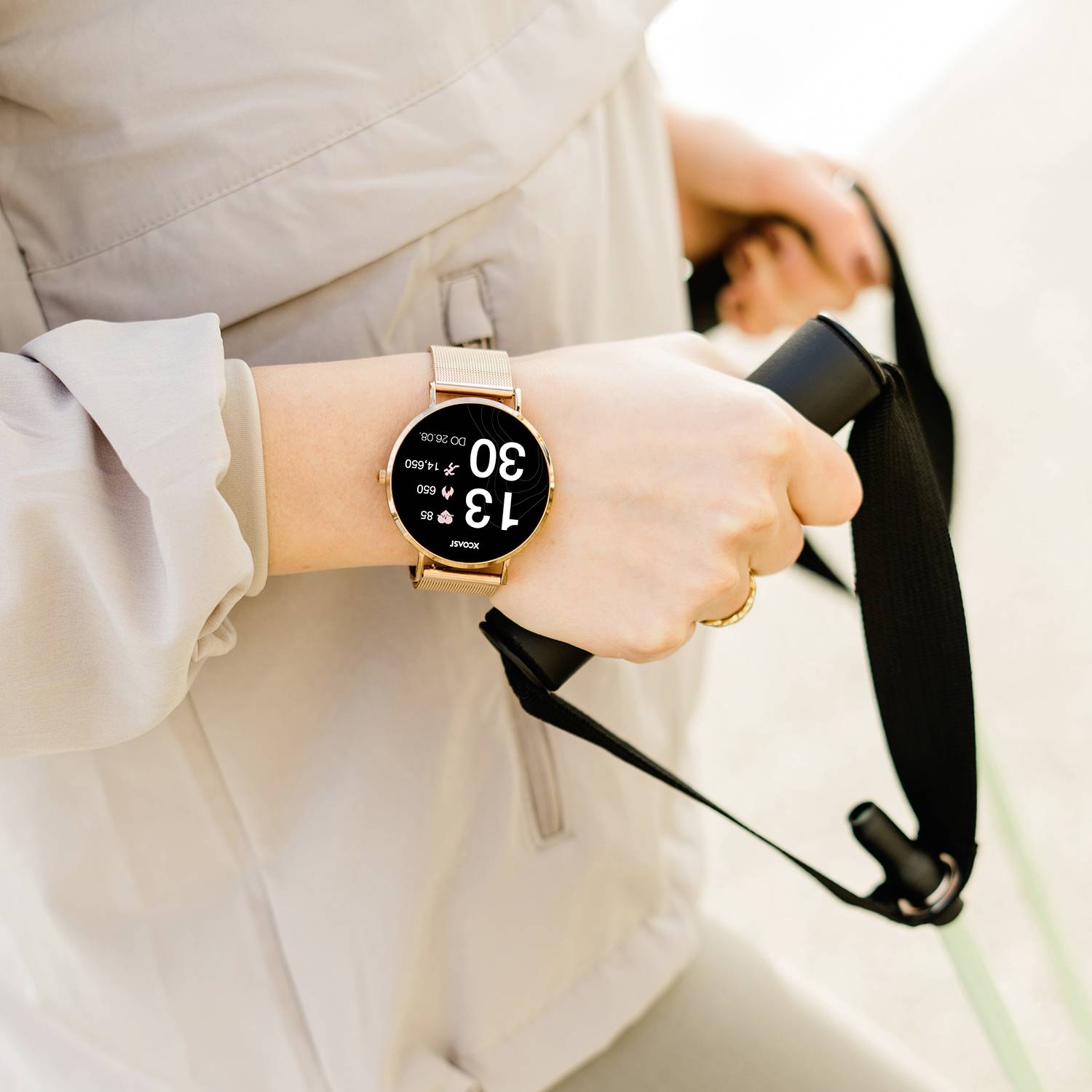 Une personne porte une montre connectée dont l'écran affiche 13:00. La personne tient un bracelet de caméra noir.