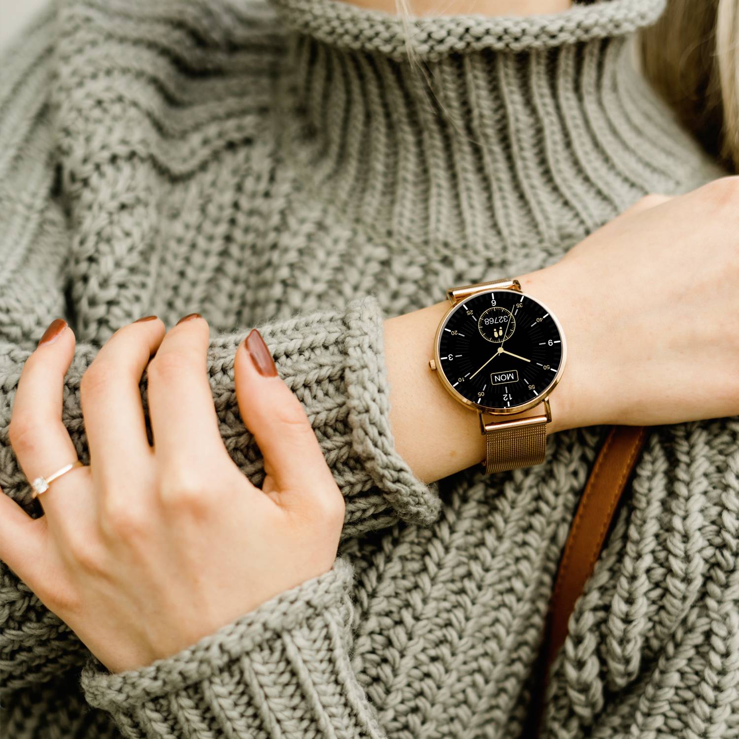Une personne porte un pull en tricot gris et montre une montre-bracelet élégante avec un cadran noir et des détails dorés.