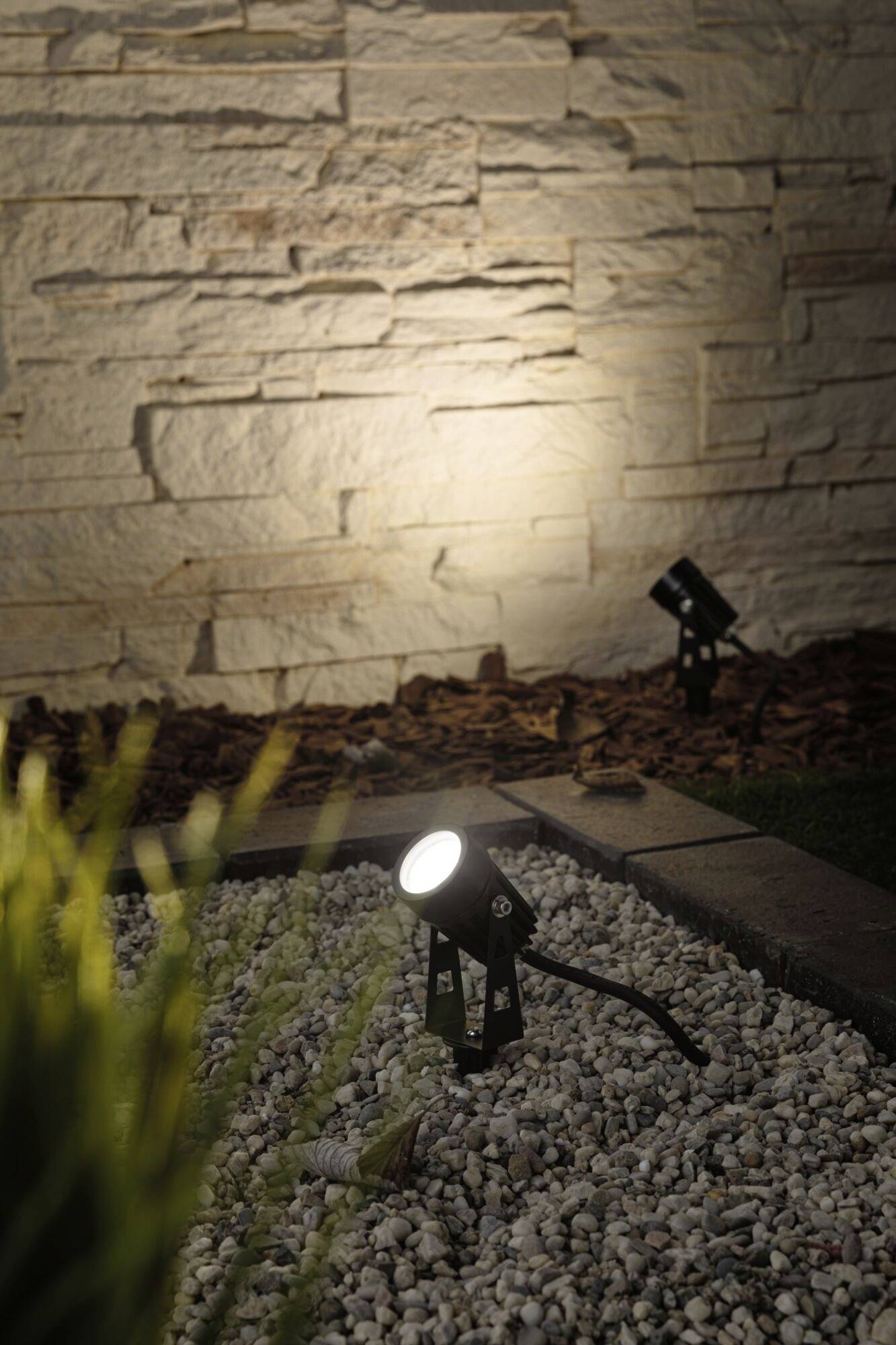 Les luminaires extérieurs illuminent le jardin avec son mur de pierre, mettent en valeur les plantes et créent une atmosphère chaleureuse et accueillante.