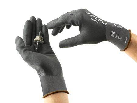 Deux mains gantées de noir tiennent un petit engrenage. Les gants sont adaptés aux travaux de précision.