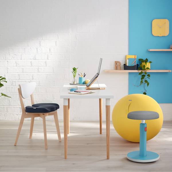 Un bureau lumineux et moderne avec une table, un ordinateur portable, un ballon de gym jaune, une chaise et des étagères sur un mur blanc et bleu.