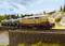 Une locomotive modèle avec deux wagons-citernes sur un pont dans un paysage. La locomotive est peinte dans la livrée rouge et beige de la DB.