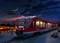 Un train de transport urbain rouge est stationné sur le quai dans la lumière du soir, sous un ciel nocturne clair avec un fin croissant de lune.