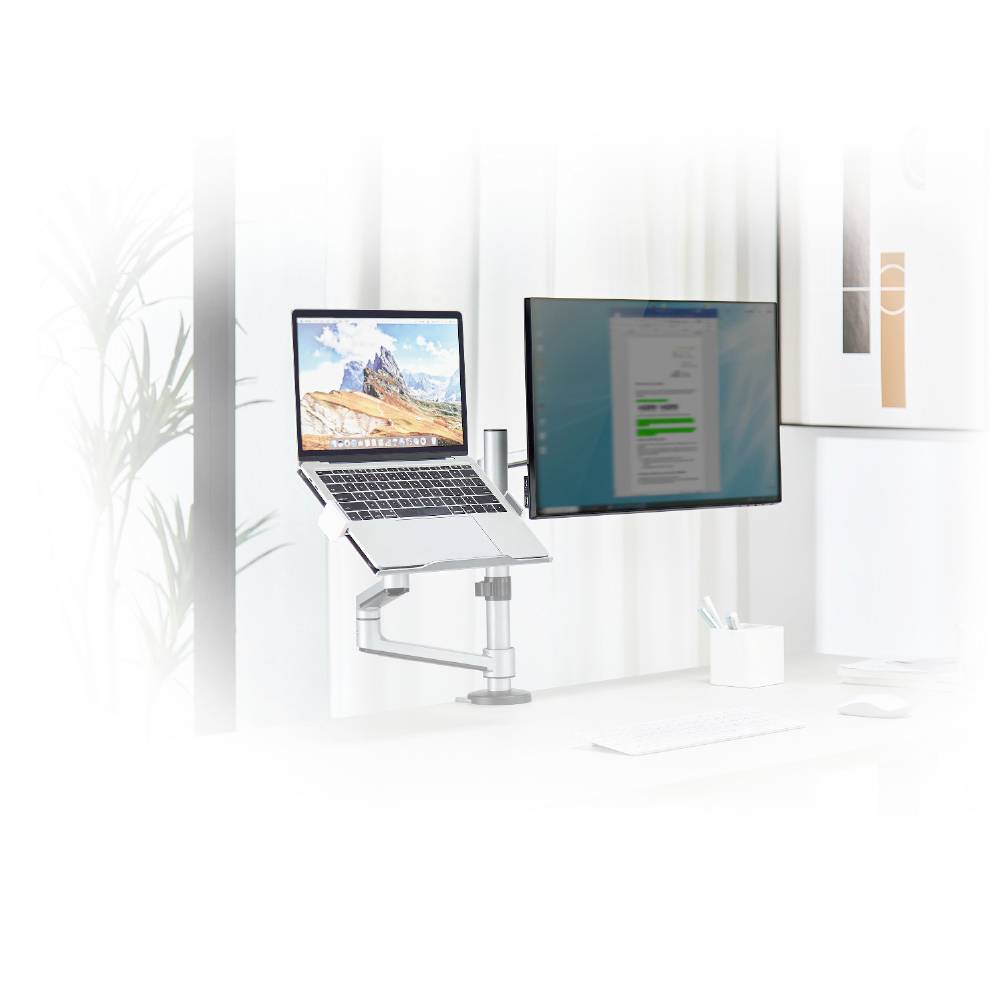 Un bureau avec un ordinateur portable sur un support réglable et un écran à côté. Des rideaux sont visibles en arrière-plan.