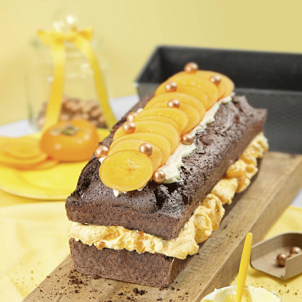Un gâteau au chocolat avec de la crème fouettée, décoré de tranches d'orange et de boules dorées, servi sur une planche en bois.