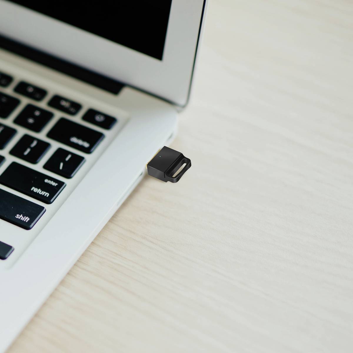 Un ordinateur portable avec une clé USB noire branchée dans un port USB. Le couvercle de l'ordinateur portable est ouvert.