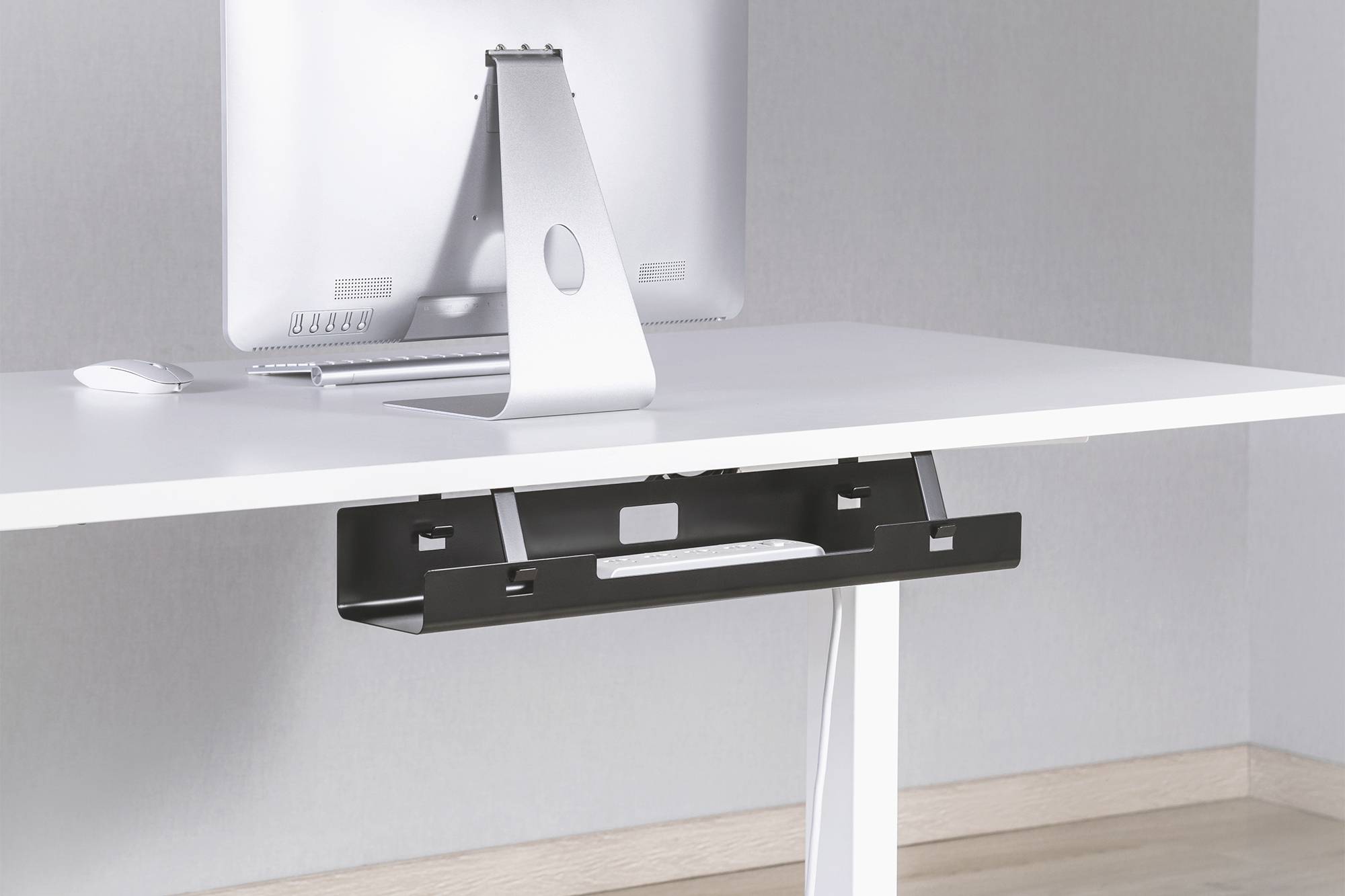 Un écran d'ordinateur sur un bureau blanc. Un canal de câbles noir est installé en dessous, dissimulant soigneusement les câbles.