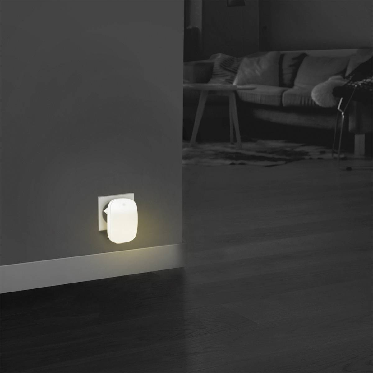 Une petite veilleuse brille sur le mur dans une pièce sombre avec un canapé en arrière-plan.