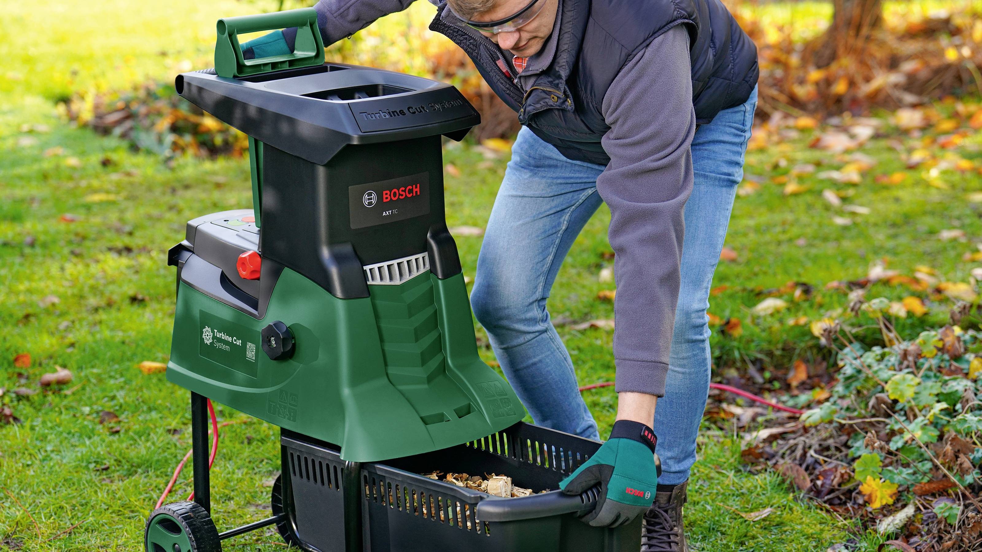Une personne vide un conteneur rempli de déchets de jardin broyés provenant d'un broyeur vert dans un jardin.
