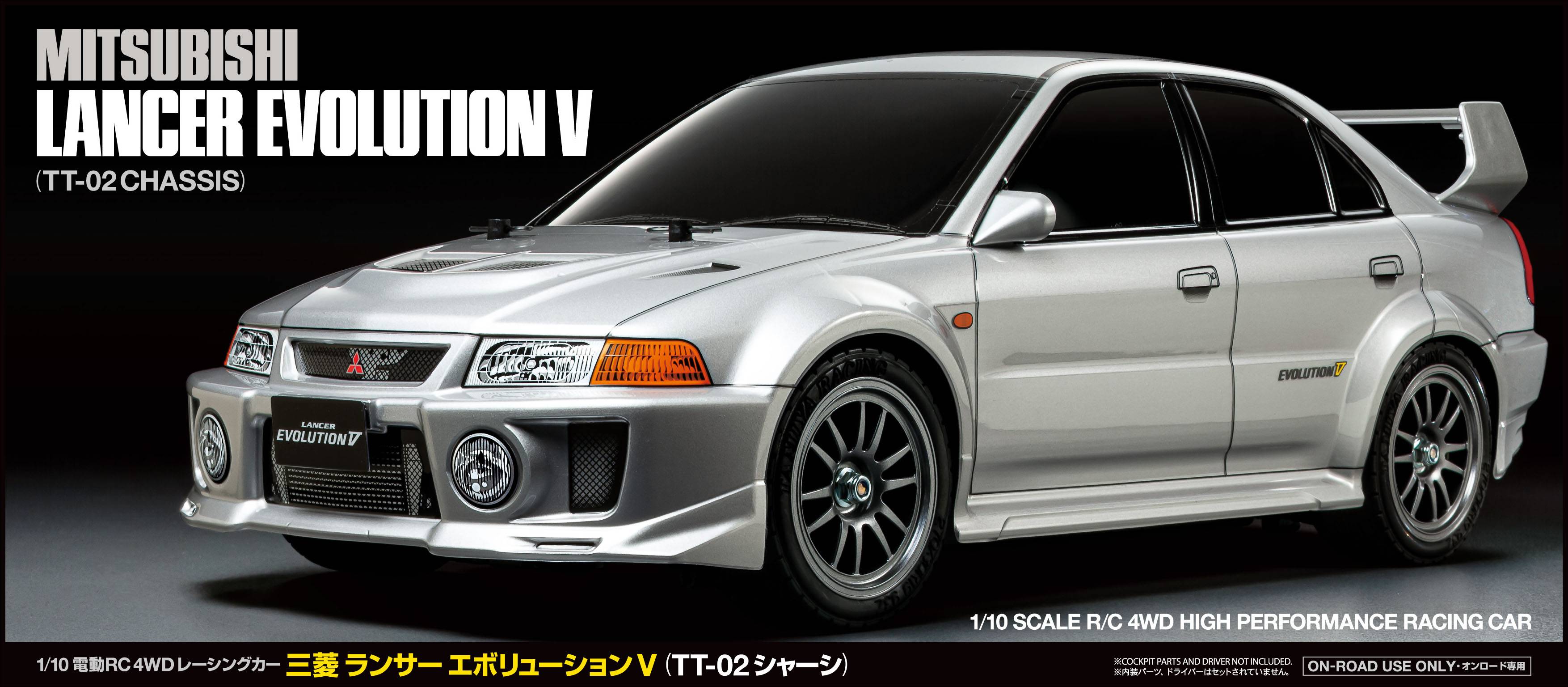 Un Mitsubishi Lancer Evolution V argenté en version de course, avec des ailettes aérodynamiques marquantes et des autocollants, présenté sur un fond noir.