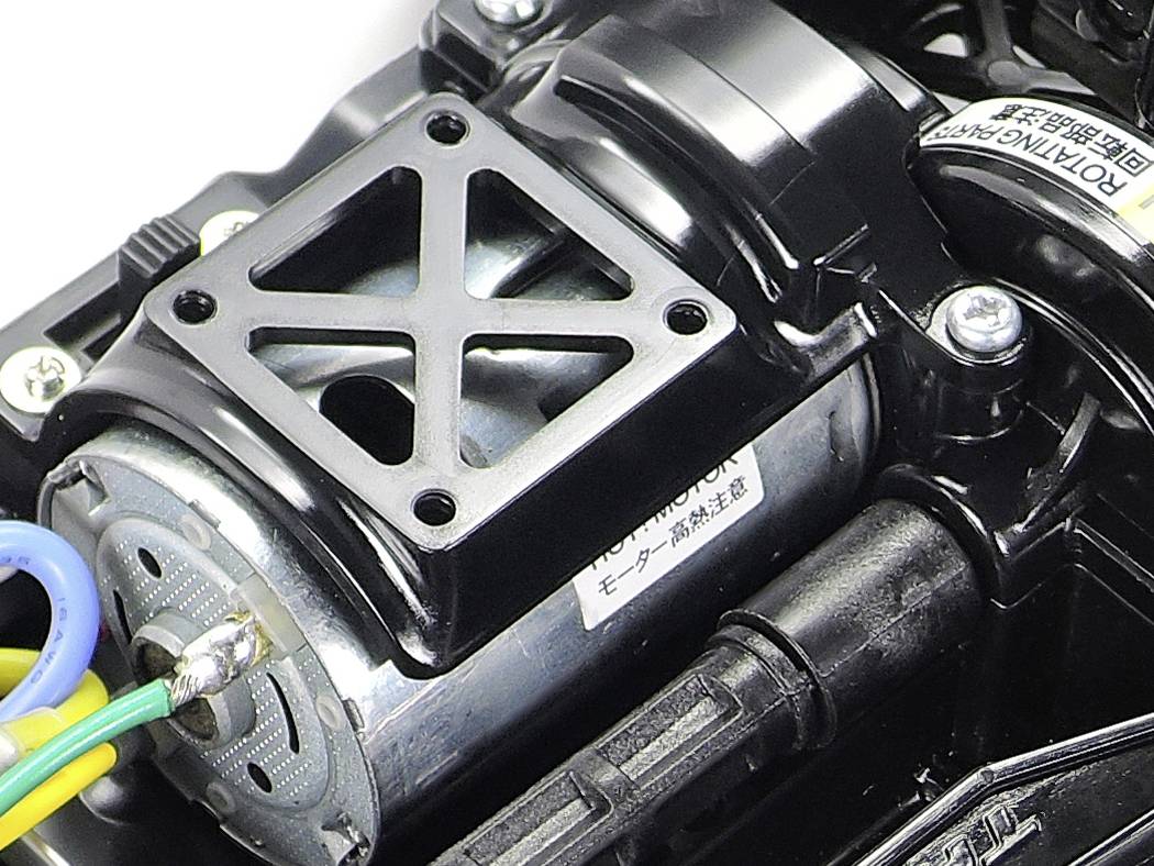 Gros plan d'un moteur électrique avec des câbles apparents et un boîtier métallique, monté sur une base en plastique noir.