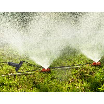 Un arroseur automatique irrigue un gazon vert en plein jour, répartissant uniformément des jets d'eau.