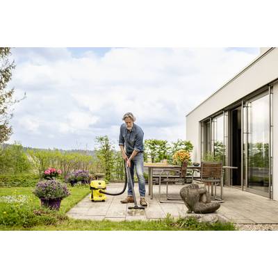 Un homme nettoie une terrasse avec un aspirateur eau et poussière jaune. Des plantes et des meubles de jardin sont visibles en arrière-plan.
