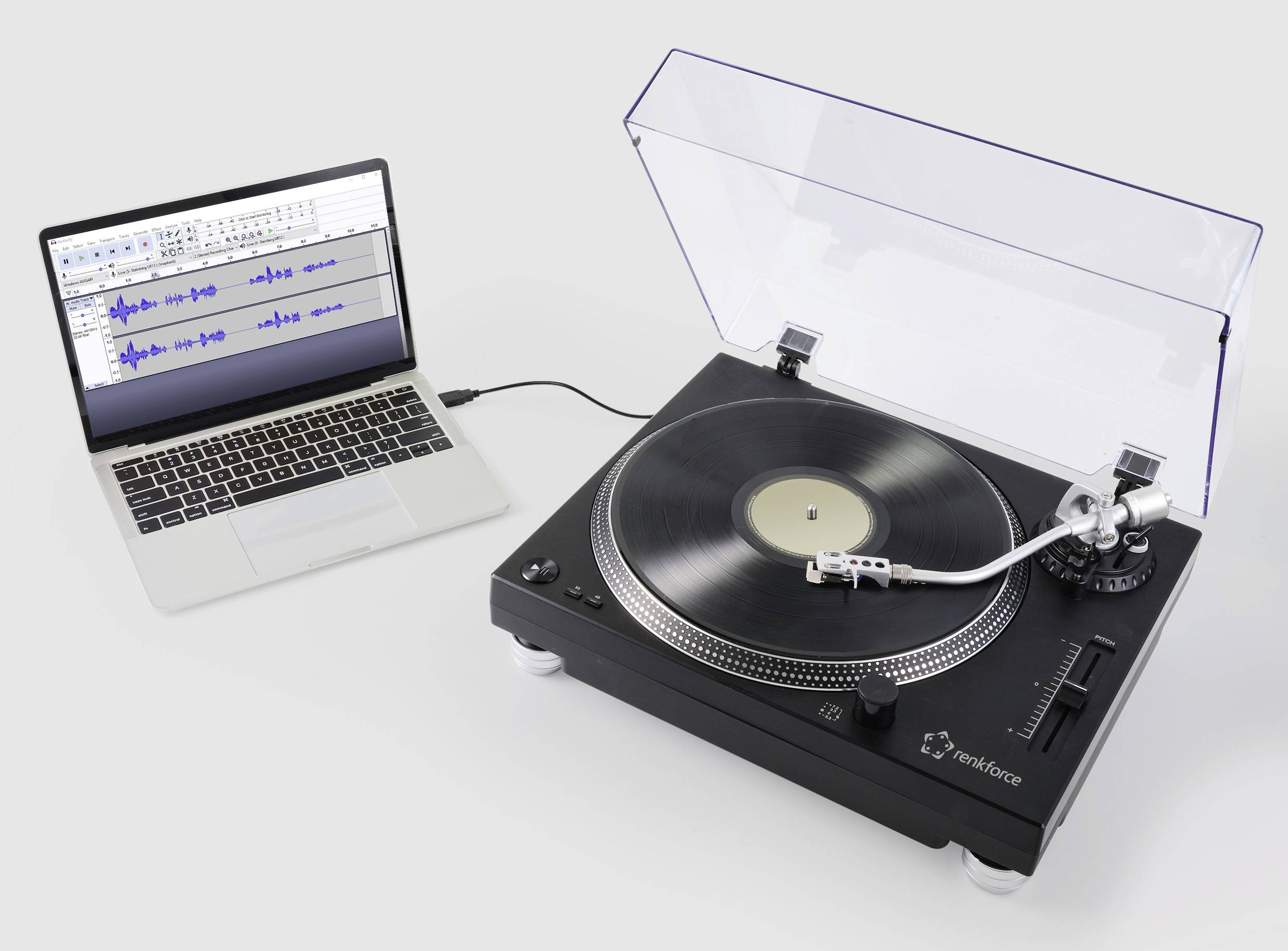Une platine vinyle est connectée à un ordinateur portable par un câble, et à l'écran s'affichent des ondes audio dans un logiciel de montage.