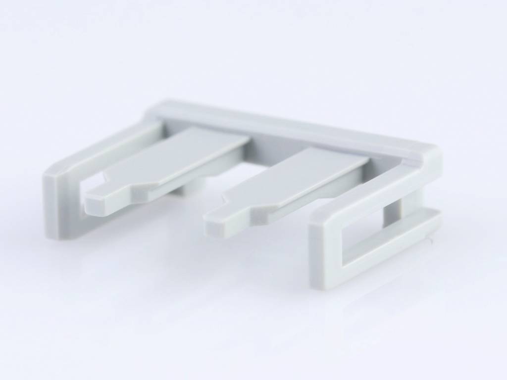 Pièce en plastique grise à trois pointes sur fond blanc. Composant possible d'un appareil ou d'une machine plus grand.