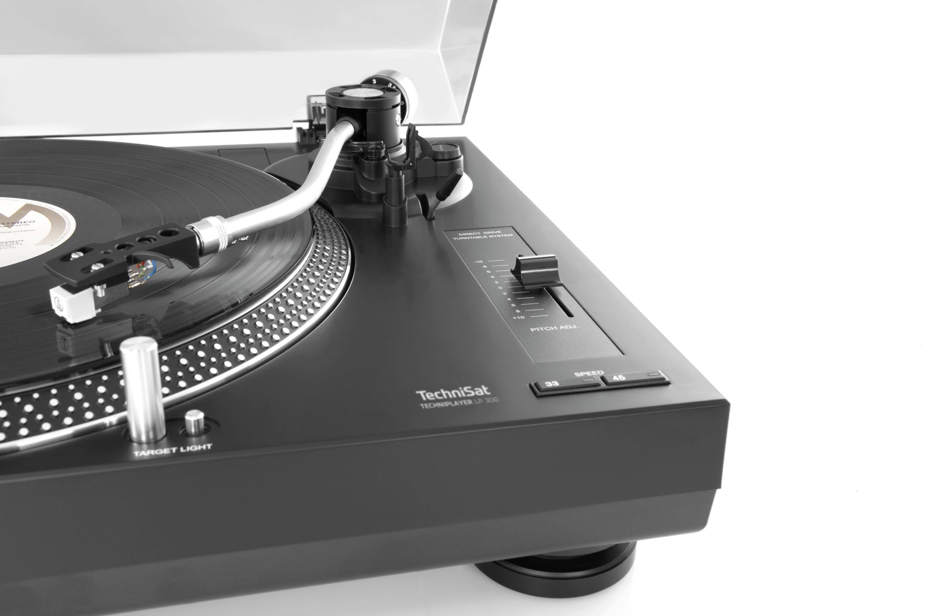 Gros plan d'un tourne-disque avec un disque vinyle noir. Le bras de lecture est dirigé vers le disque. En arrière-plan, on peut voir un couvercle ouvert.