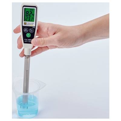 Une main tient un pH-mètre numérique plongé dans un gobelet contenant un liquide bleu. L'écran affiche un pH de 8,24 et une température de 23,7°C.