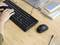 Des mains tapent sur un clavier posé sur un bureau, avec une souris, des stylos et des cahiers à proximité.