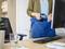 Une personne range une souris dans un sac pour ordinateur portable bleu sur un bureau où se trouvent également un écran, un clavier et un verre. Environnement de bureau.