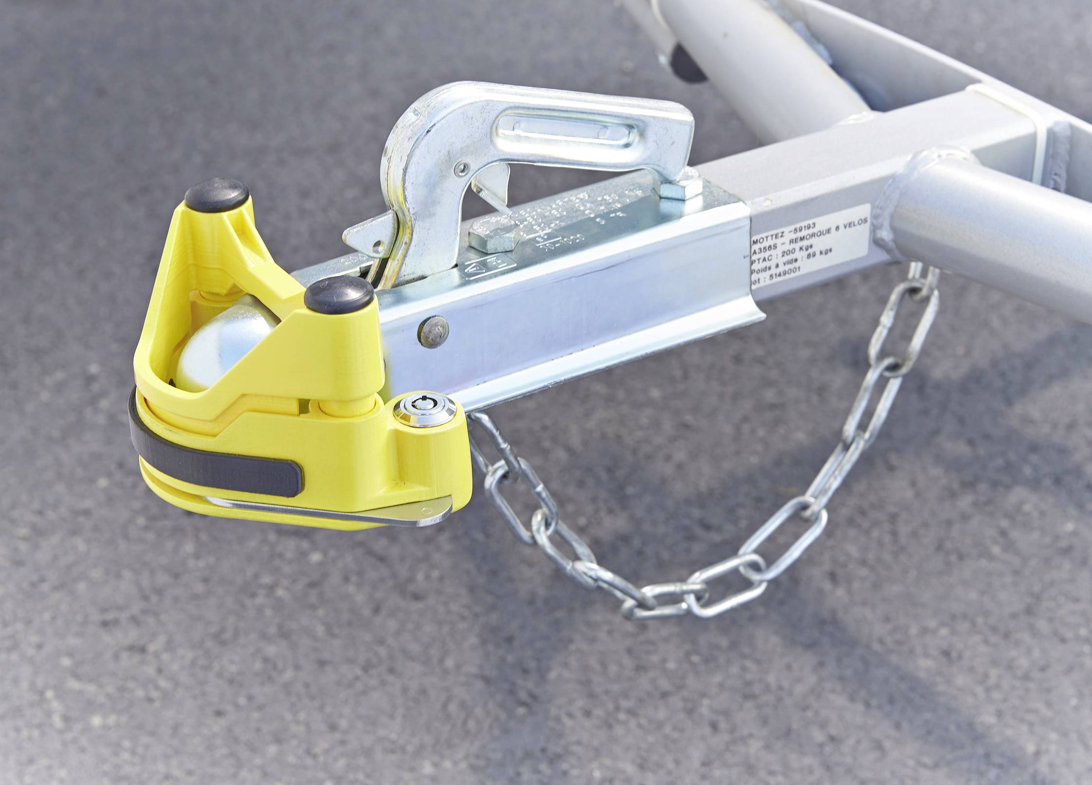 Un verrou d'attelage jaune est fixé sur un châssis de remorque. Une chaîne de sécurité est attachée au châssis.