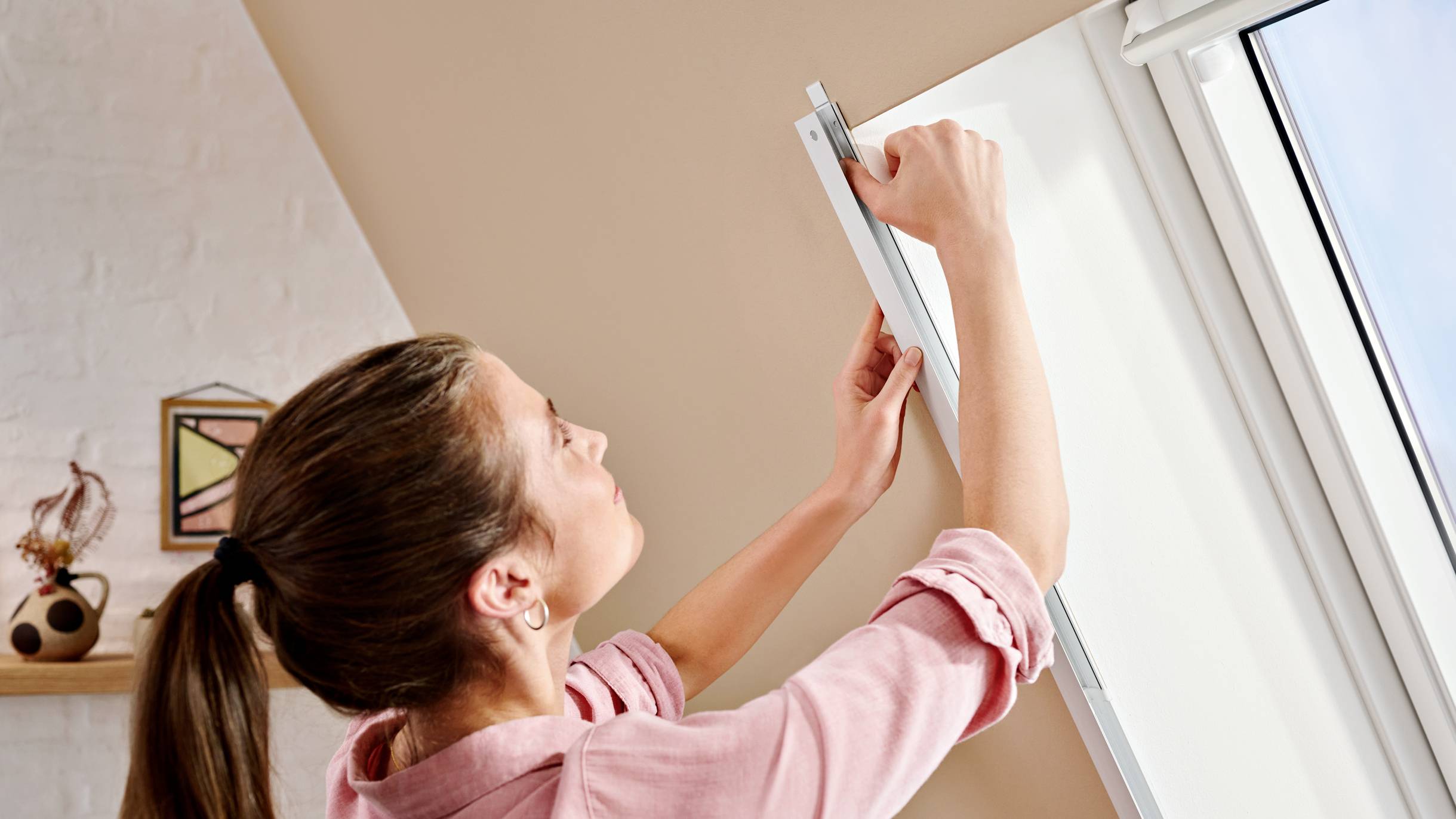 Une personne fixe un protège-lumière à une fenêtre dans une pièce.