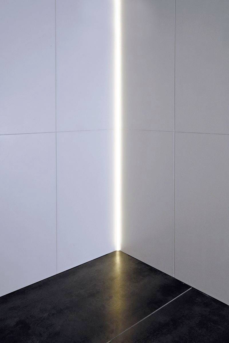 Une pièce au sol sombre et aux murs blancs ; une ligne lumineuse verticale dans le coin crée un look moderne et minimaliste.