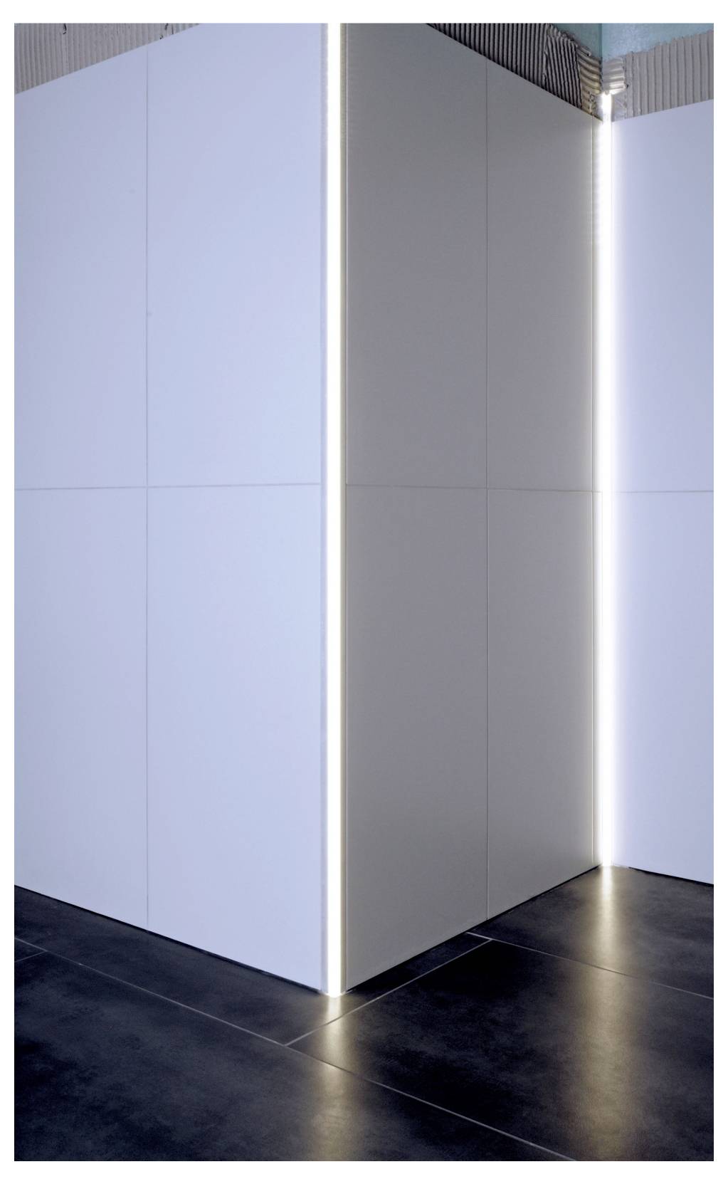Coin intérieur moderne avec des panneaux muraux blancs et des bandes lumineuses verticales au-dessus d'un sol carrelé sombre.
