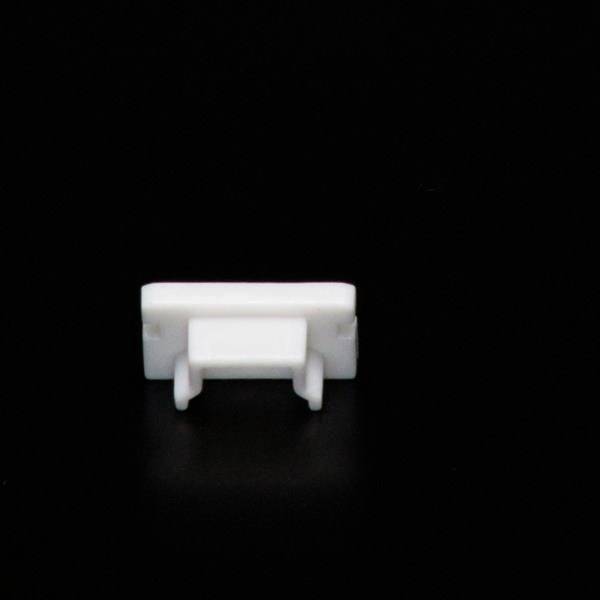 Un clip en plastique blanc unique sur un fond noir, probablement destiné à la gestion des câbles ou à la fixation.