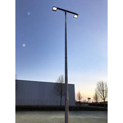 Un lampadaire élevé se dresse sur une place à côté d'un bâtiment moderne. Le ciel, au crépuscule, est clair avec quelques nuages.