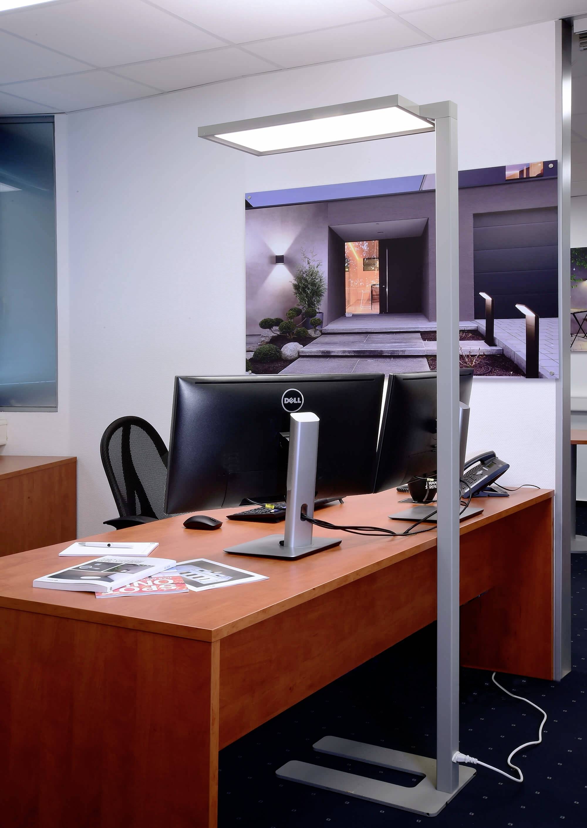 Espace de bureau moderne avec un bureau en bois, un ordinateur, un téléphone et une lampe sur pied. Un tableau représentant une maison illuminée la nuit est accroché au mur.