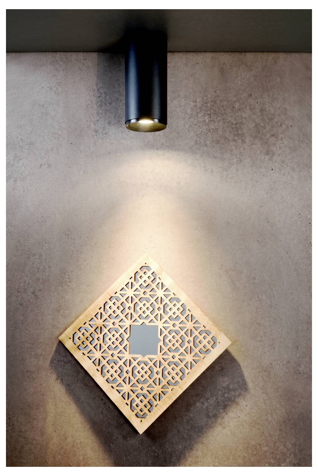 Un spot noir monté au mur éclaire un panneau décoratif en treillis en forme de losange sur un mur gris texturé.