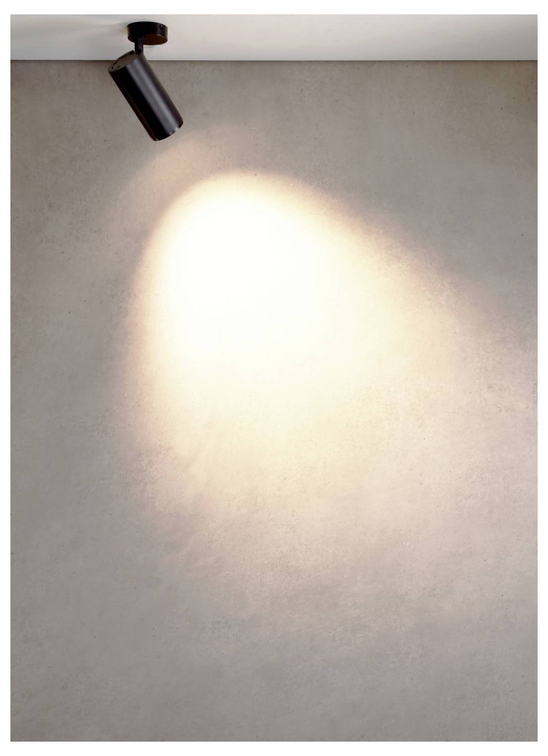 Un spot noir au plafond projette un faisceau lumineux ovale et vif sur un mur gris uni.