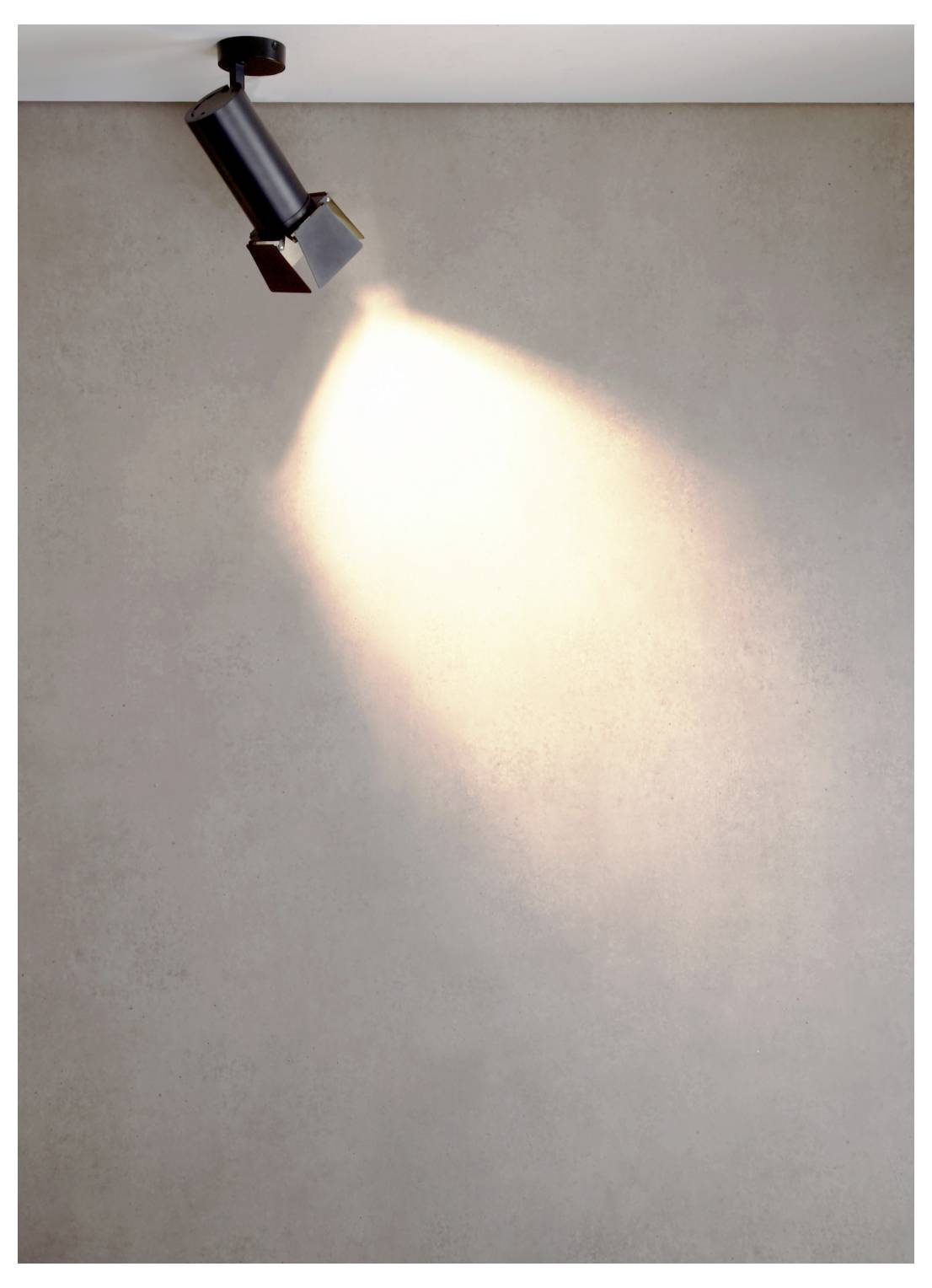 Un spot monté au plafond projette un faisceau de lumière vive sur un mur uni.