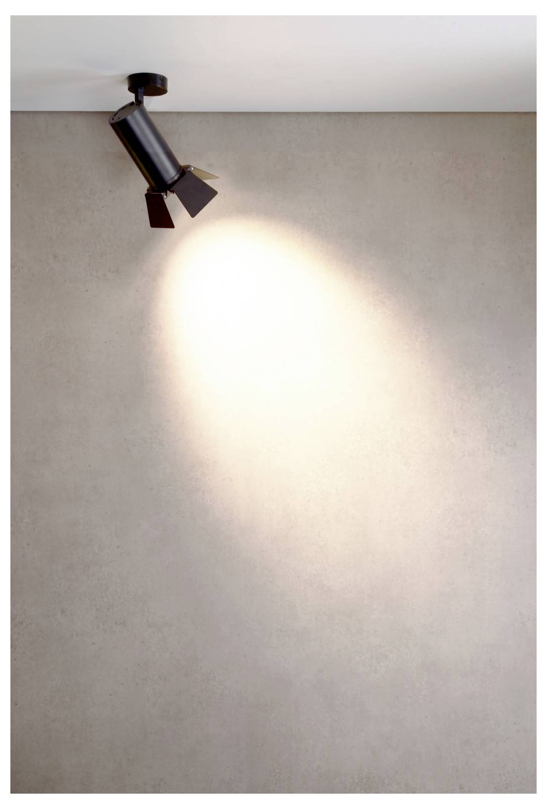 Un spot de plafond noir projette un faisceau de lumière chaude sur un mur beige uni.