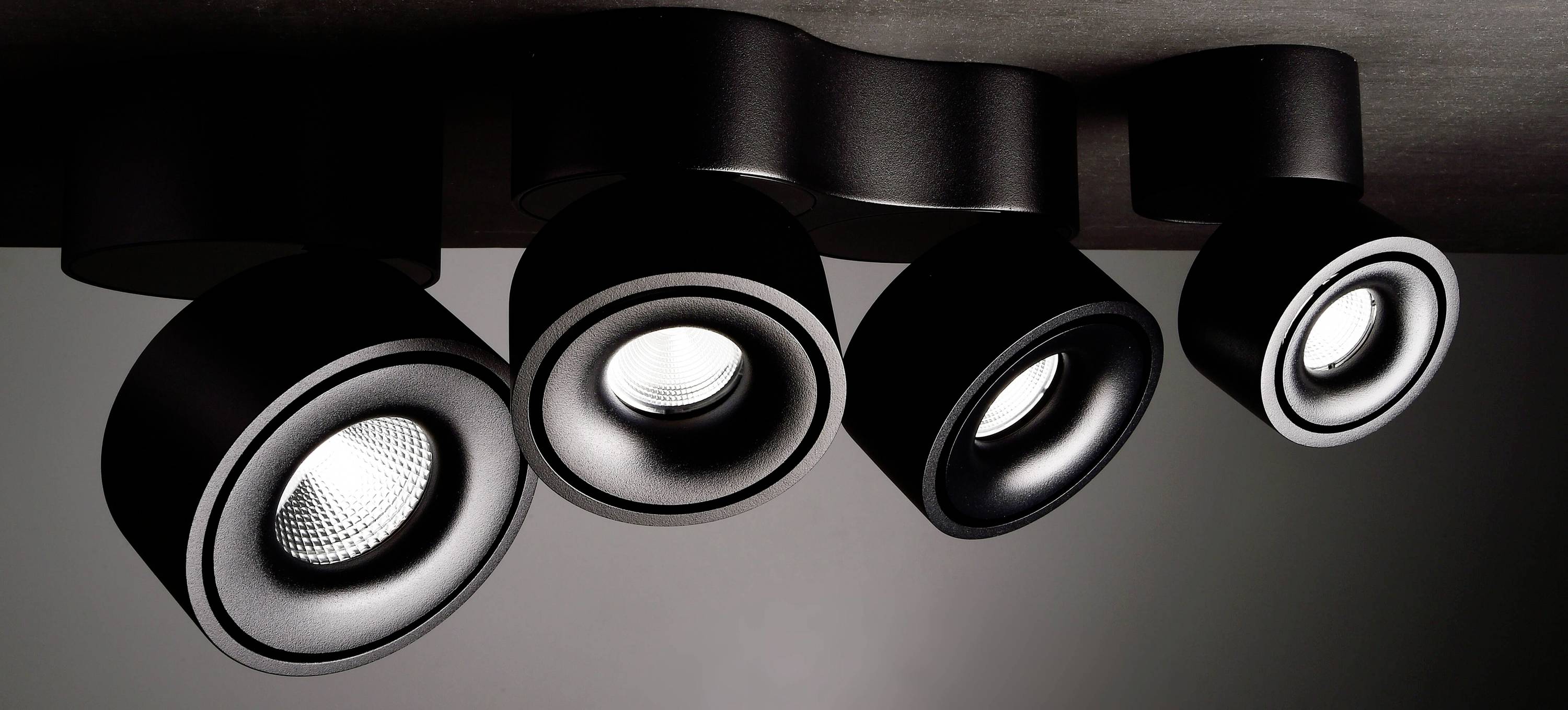 Quatre spots de plafond LED noirs, au design moderne et élancé, sont suspendus à partir d'un support aux lignes ondulantes.