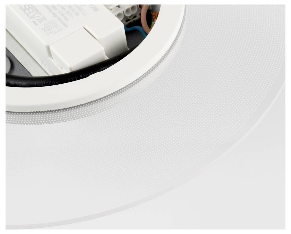 Gros plan d'un spot encastré blanc au plafond, avec le boîtier et le câblage visibles par l'ouverture.