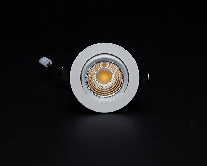 Un spot LED rond argenté avec un noyau lumineux orange, intégré dans un support de plafond, sur un fond noir.
