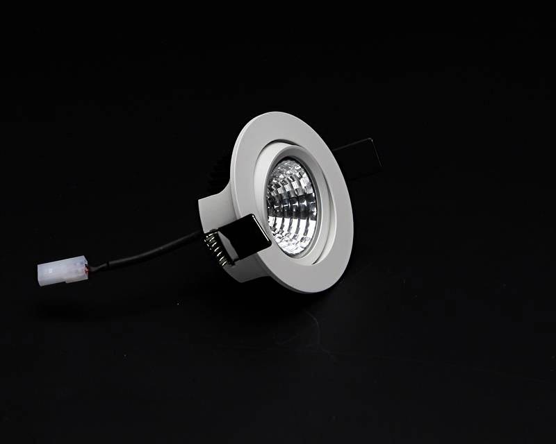 Luminaire encastrable rond argenté avec câble électrique sur un fond noir.