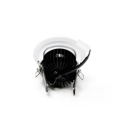 Un luminaire encastré de plafond à LED en métal et en plastique, avec un cadre rond et des ailettes de refroidissement, est posé à l'envers sur une surface blanche.