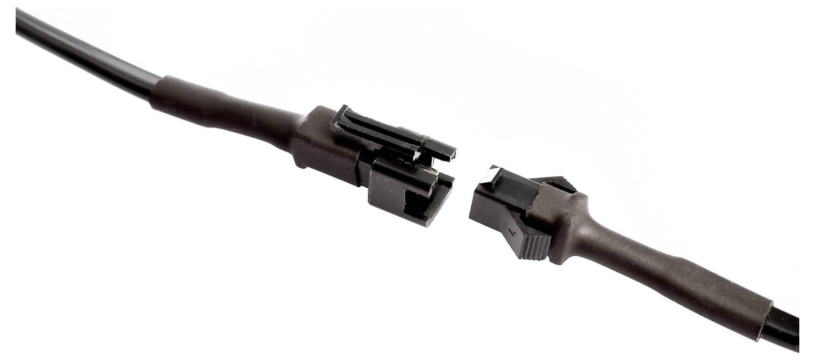 Gros plan de deux connecteurs de câbles électriques noirs déconnectés, avec des extrémités dénudées, sur fond blanc.