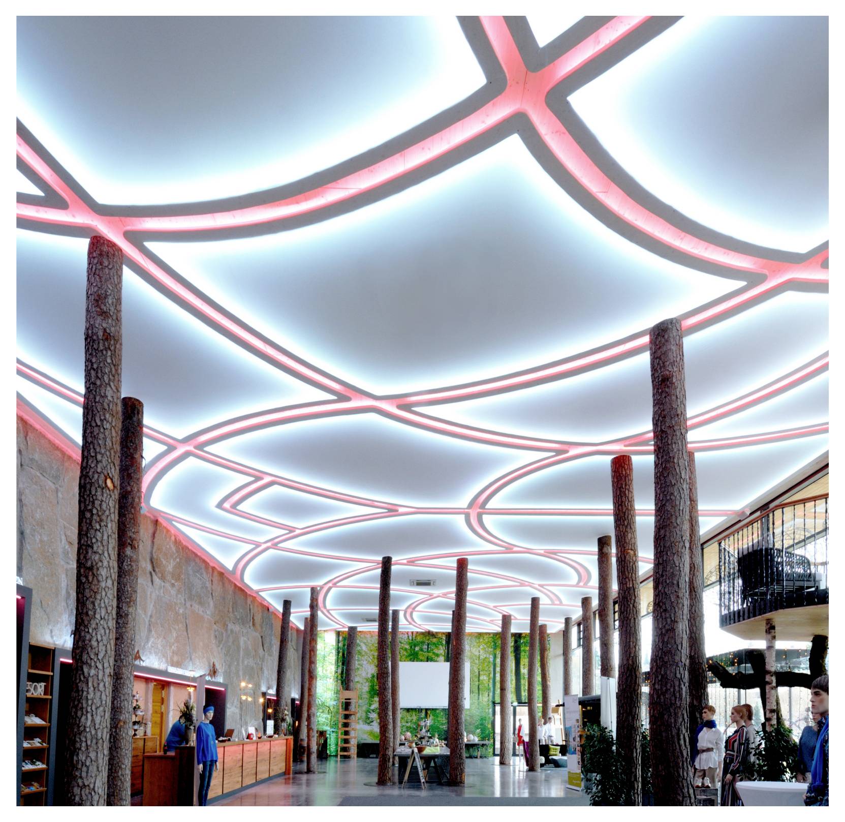 Atrium intérieur moderne avec un plafond en treillis aux reflets rose et bleu lumineux, de hautes colonnes en bois et quelques personnes dans un hall spacieux.